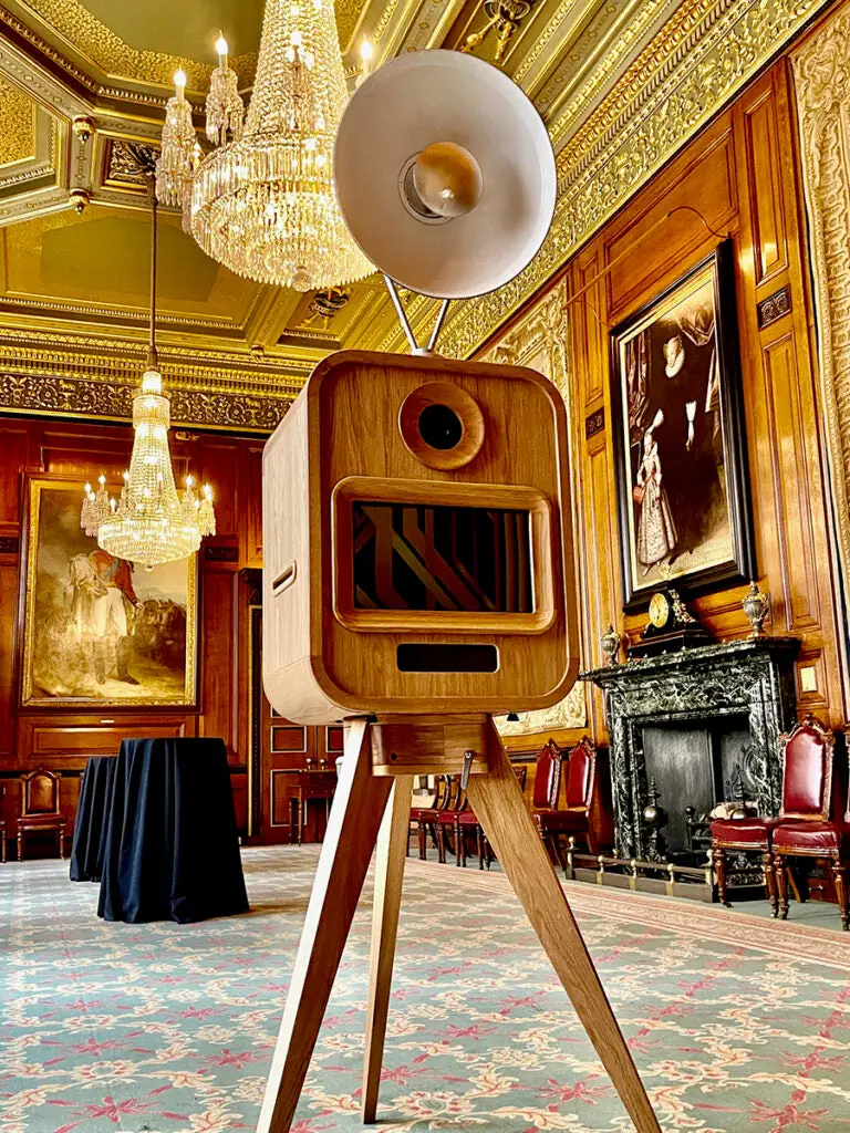 Oak vintage photo booth on wooden tripod legs in a panelled London reception room with chandeliers